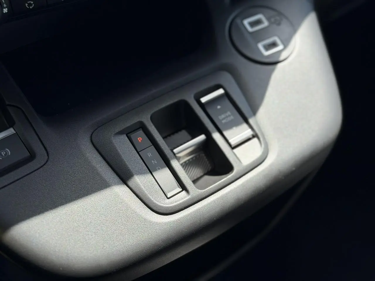 Gros plan sur la console centrale grise du Citroën Berlingo ë-136 avec commandes de boîte automatique et frein de stationnement.