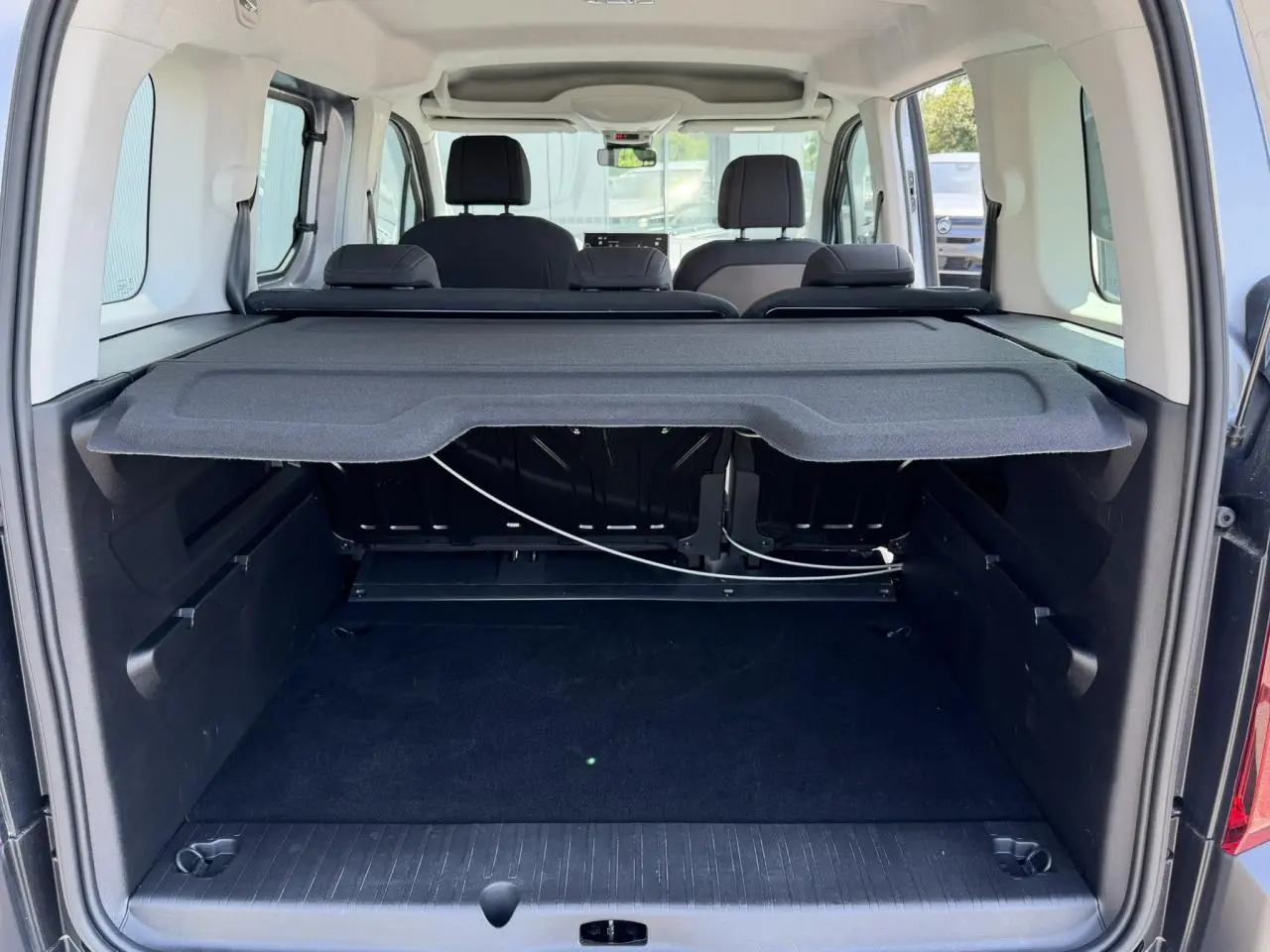 Coffre ouvert d’un Citroën Berlingo ë-136 gris Artense, vue arrière montrant la tablette cache-bagages et les sièges noirs.