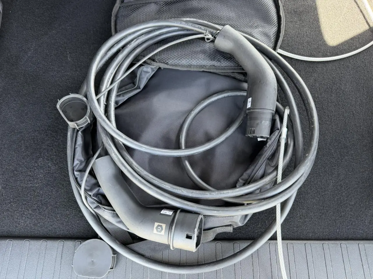 Câble de recharge électrique noir enroulé dans le coffre d’un Citroën Berlingo gris Artense, vue de dessus.
