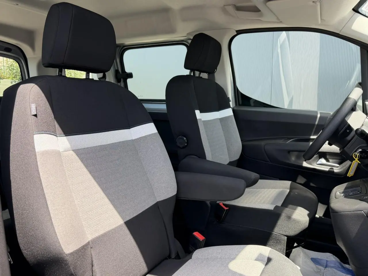 Vue intérieure côté conducteur du Citroën Berlingo 2025, sièges tissu bicolore gris et noir avec accoudoirs.
