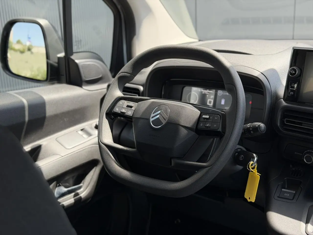 Vue intérieure centrée sur le volant multifonction du Citroën Berlingo ë-136 gris Artense, tableau de bord et rétro gauche visibles.