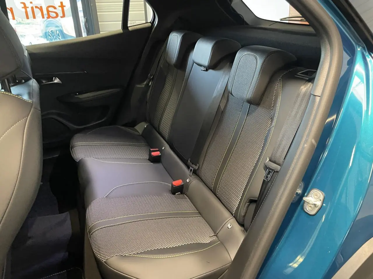 Vue intérieure côté gauche sur la banquette arrière en tissu et cuir noir avec surpiqûres vertes d’un Peugeot 2008 bleu.