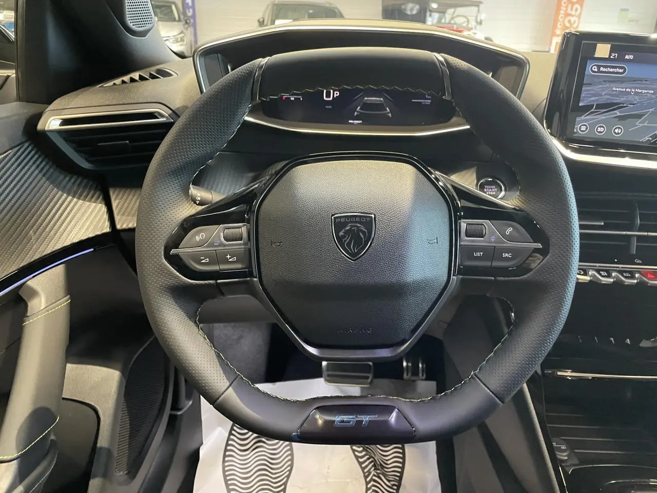 Volant compact cuir noir avec logo Peugeot et badge GT, tableau de bord numérique et partie centrale de la planche de bord.