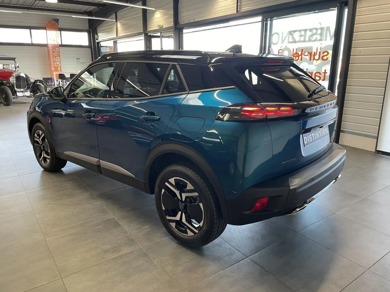 Peugeot 2008 hybride bleu vue 3/4 arrière droit en intérieur avec toit noir et feux LED allumés.