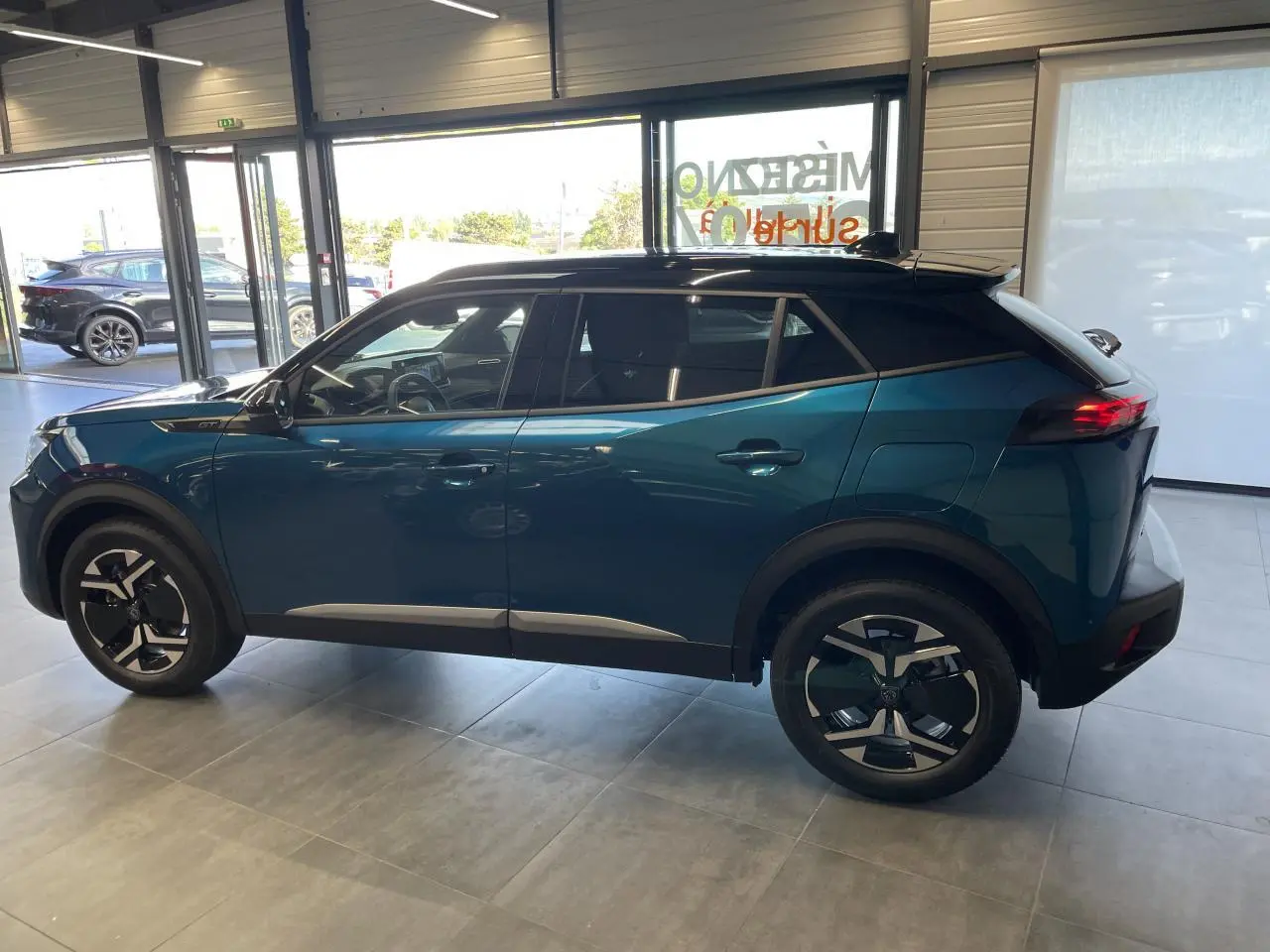 Peugeot 2008 hybride bleu vue de profil côté gauche en intérieur, avec toit noir et jantes distinctives.