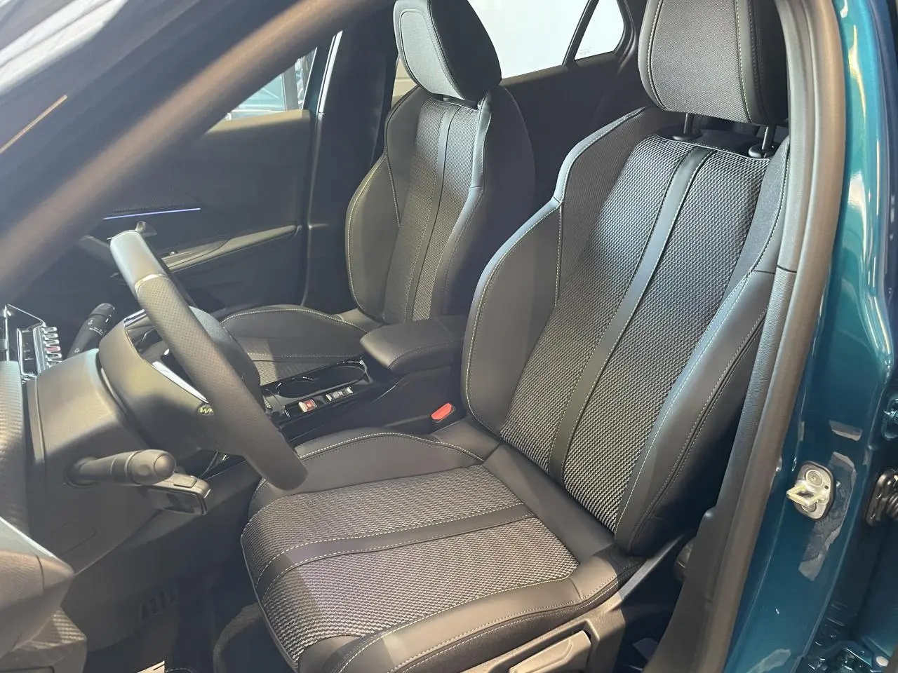 Vue intérieure côté conducteur du Peugeot 2008 bleu, montrant les sièges en tissu et cuir avec surpiqûres contrastées.