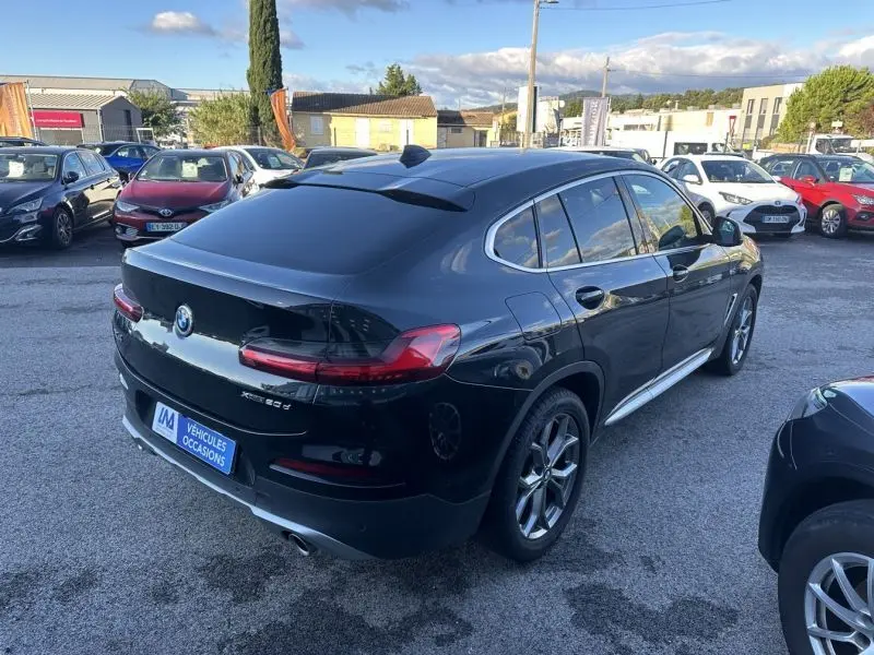 Vue 3/4 arrière droite d'un BMW X4 gris foncé X Drive 190 CV X-Line de 2019 sur un parking extérieur.