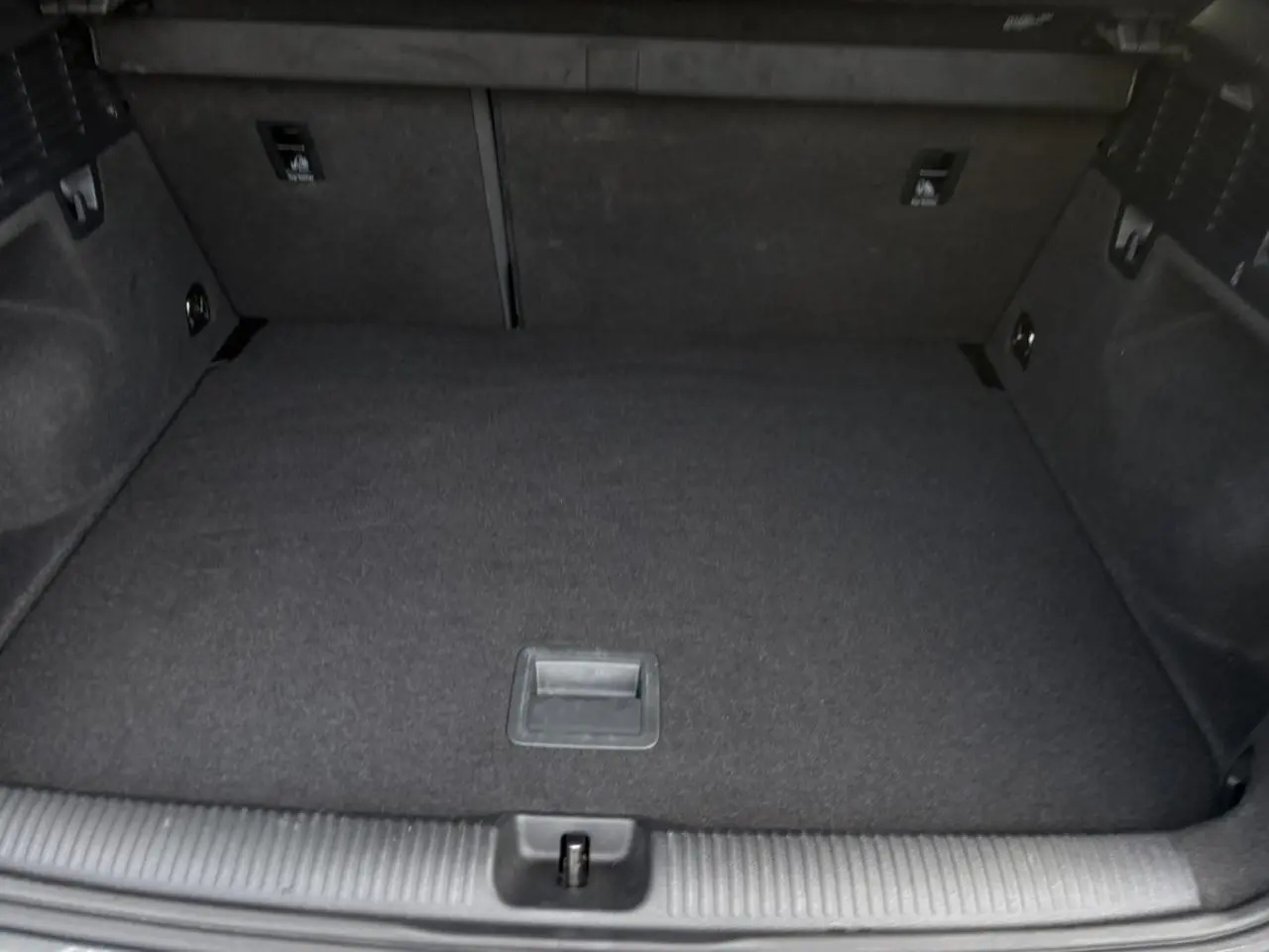 Coffre vide de l'Audi Q2 30 TDI S-Line 2025, vue intérieure arrière avec revêtement noir et espace de rangement plat.