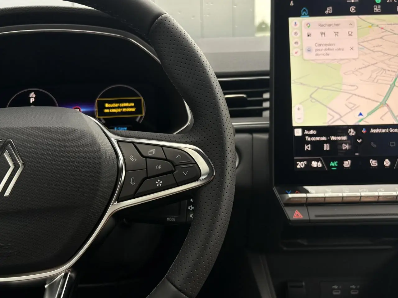 Vue rapprochée du volant perforé et du tableau de bord numérique du Renault Captur blanc nacré, avec écran tactile central affichant la navigation.