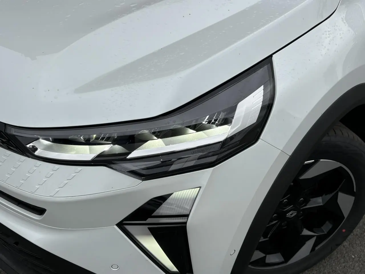 Gros plan sur l'avant droit du Renault Captur blanc nacré, mettant en valeur le phare LED Pure Vision et la jante noire.