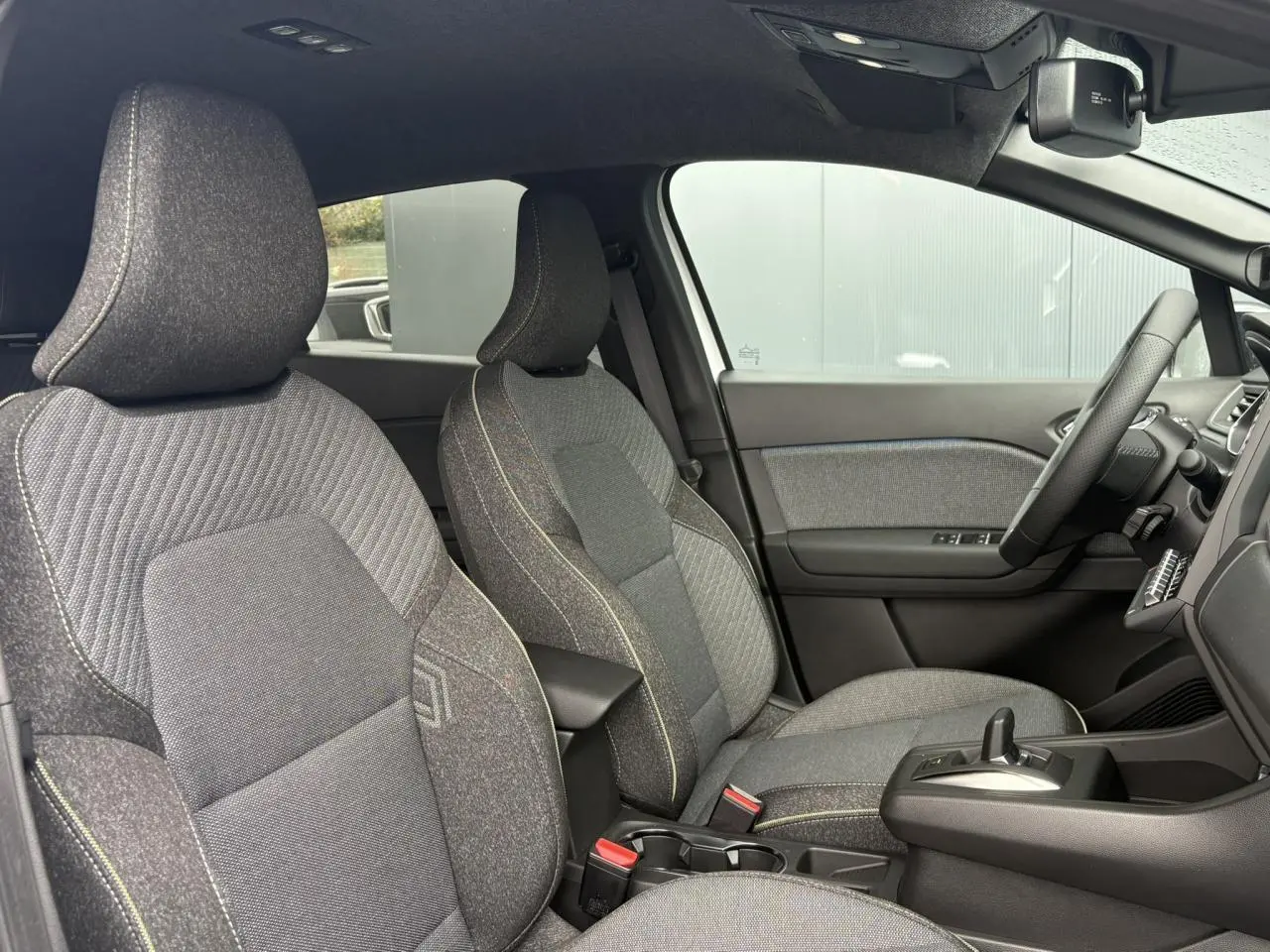 Vue intérieure côté droit du Renault Captur 2026, sièges tissu gris avec surpiqûres contrastantes et console centrale noire.