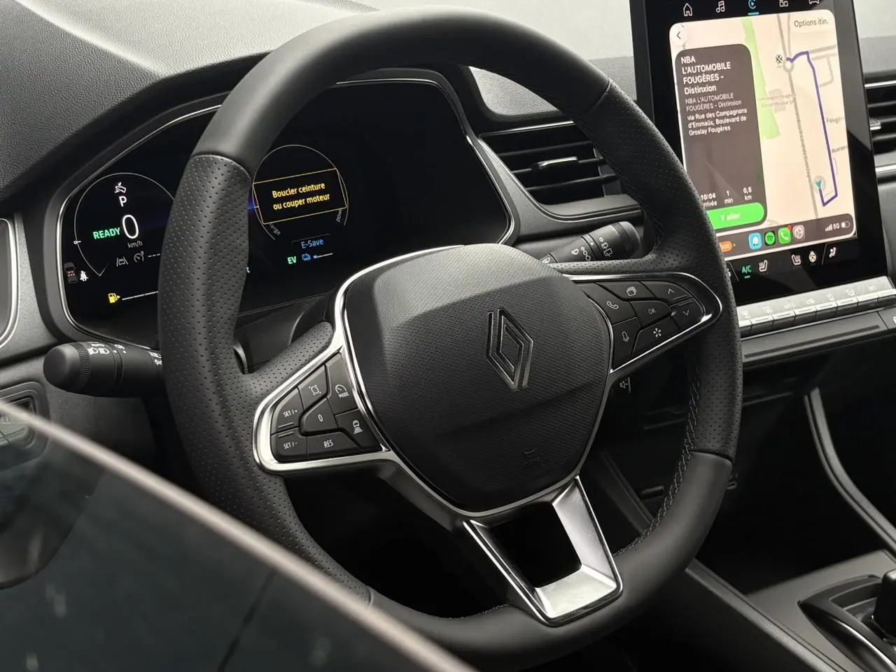 Vue rapprochée du volant noir perforé et du tableau de bord numérique du Renault Captur 2026 avec écran tactile central affichant la navigation.