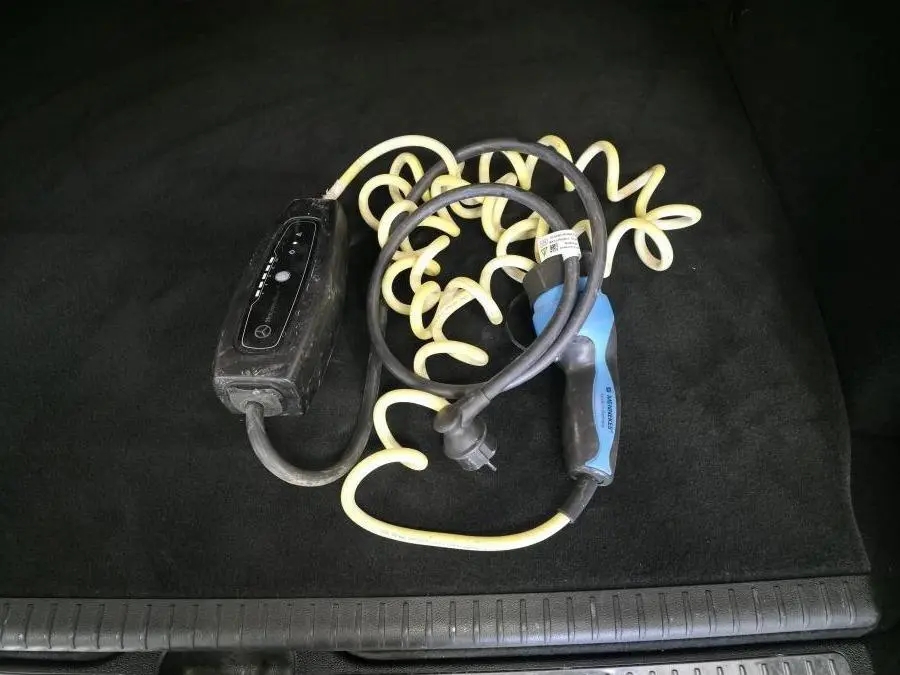 Câble de recharge hybride noir et bleu enroulé dans le coffre noir d'un Mercedes GLC 350 e gris.