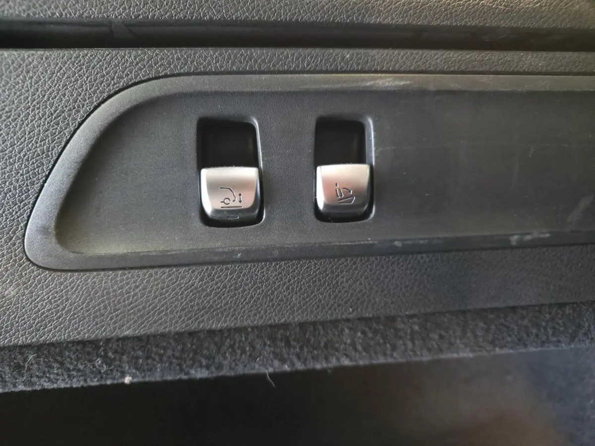 Gros plan sur les commandes argentées d'ouverture du hayon et d'abaissement des sièges dans le coffre d'un Mercedes GLC gris.