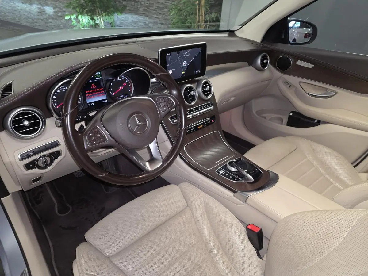 Vue intérieure avant droite du Mercedes GLC 350 e gris, avec tableau de bord en cuir marron et sièges beige perforés.