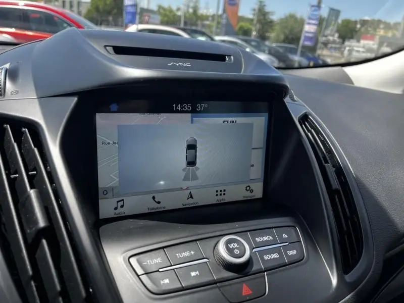 Vue intérieure du tableau de bord du Ford Kuga 2018, écran tactile SYNC avec navigation et commandes audio visibles.