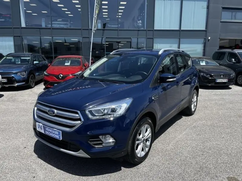 Ford Kuga bleu foncé 2018 en 3/4 avant droit, finition Titanium avec calandre chromée et toit ouvrant visible.