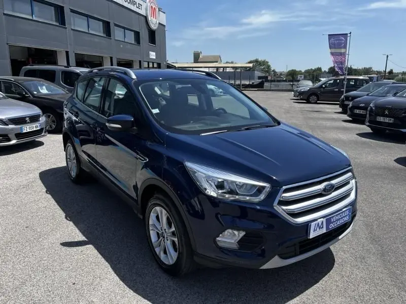 Ford Kuga bleu foncé en 3/4 avant droit, mettant en valeur la calandre chromée et les phares modernes.