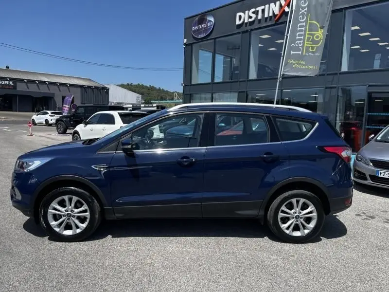 Vue de profil côté gauche d'un Ford Kuga bleu foncé 2018, version Titanium, garé devant un showroom Distinxion.