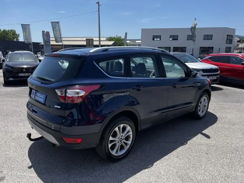 Ford Kuga 1.5 EcoBoost 2018 bleu foncé, vue 3/4 arrière droit avec barres de toit et attelage visible.
