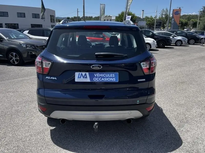 Vue arrière d'un Ford Kuga bleu foncé 2018 avec badge Titanium et attelage visible sur un parking extérieur.