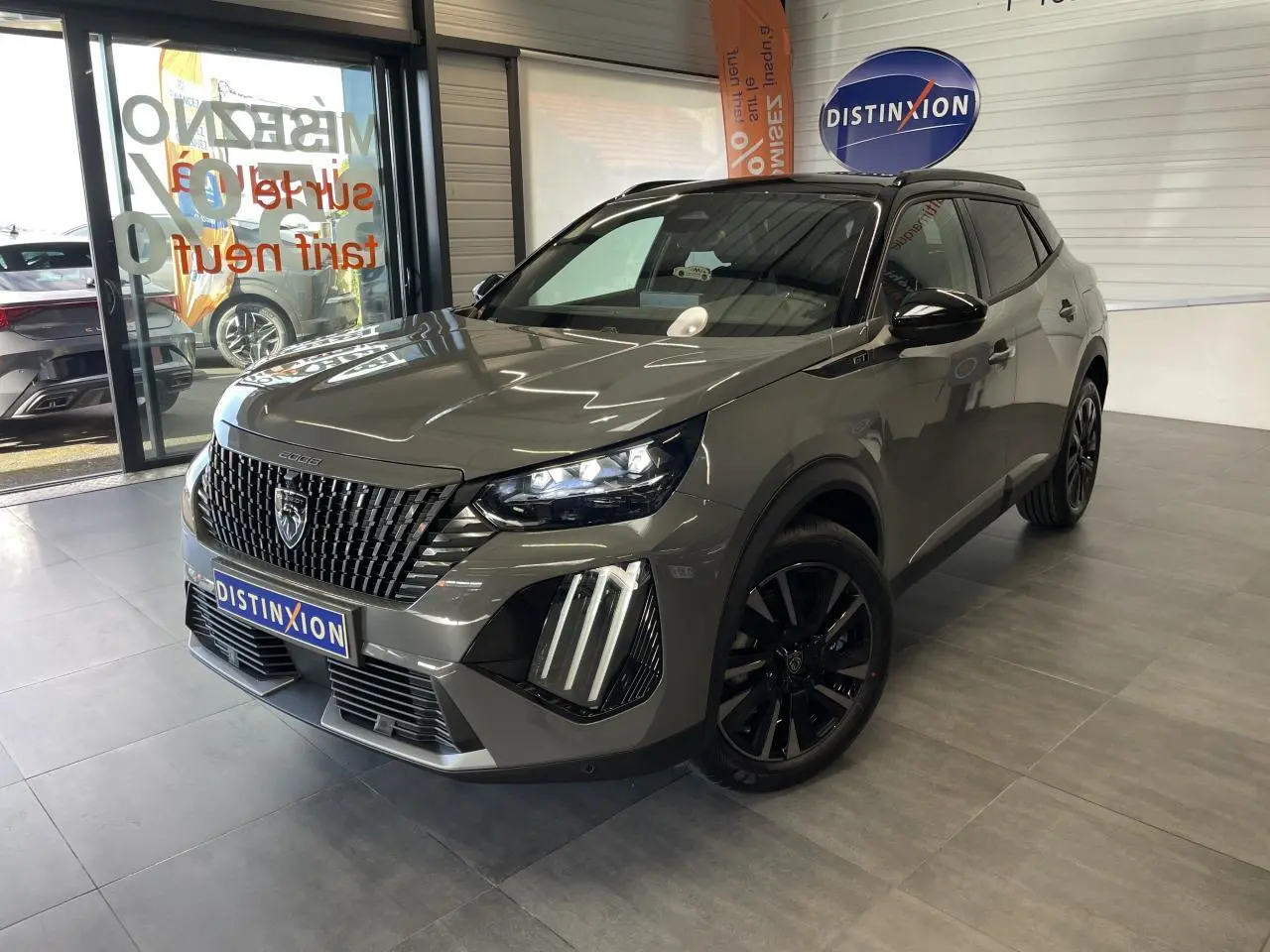 Peugeot 2008 gris en 3/4 avant droit, avec calandre noire distinctive et jantes alliage noires, en showroom.