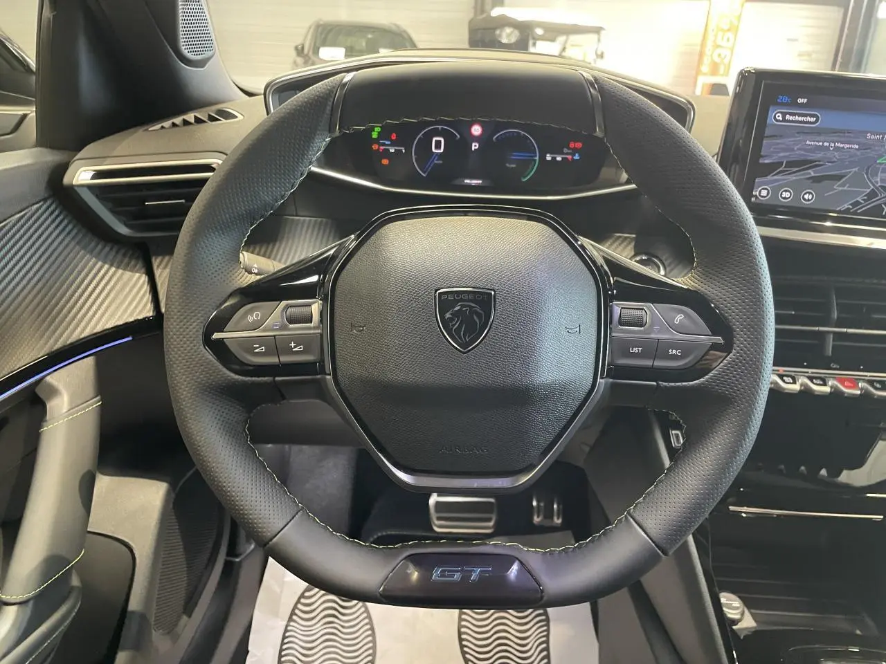 Vue centrée sur le volant cuir noir avec logo Peugeot et badge GT, tableau de bord digital et écran tactile gris du Peugeot 2008.