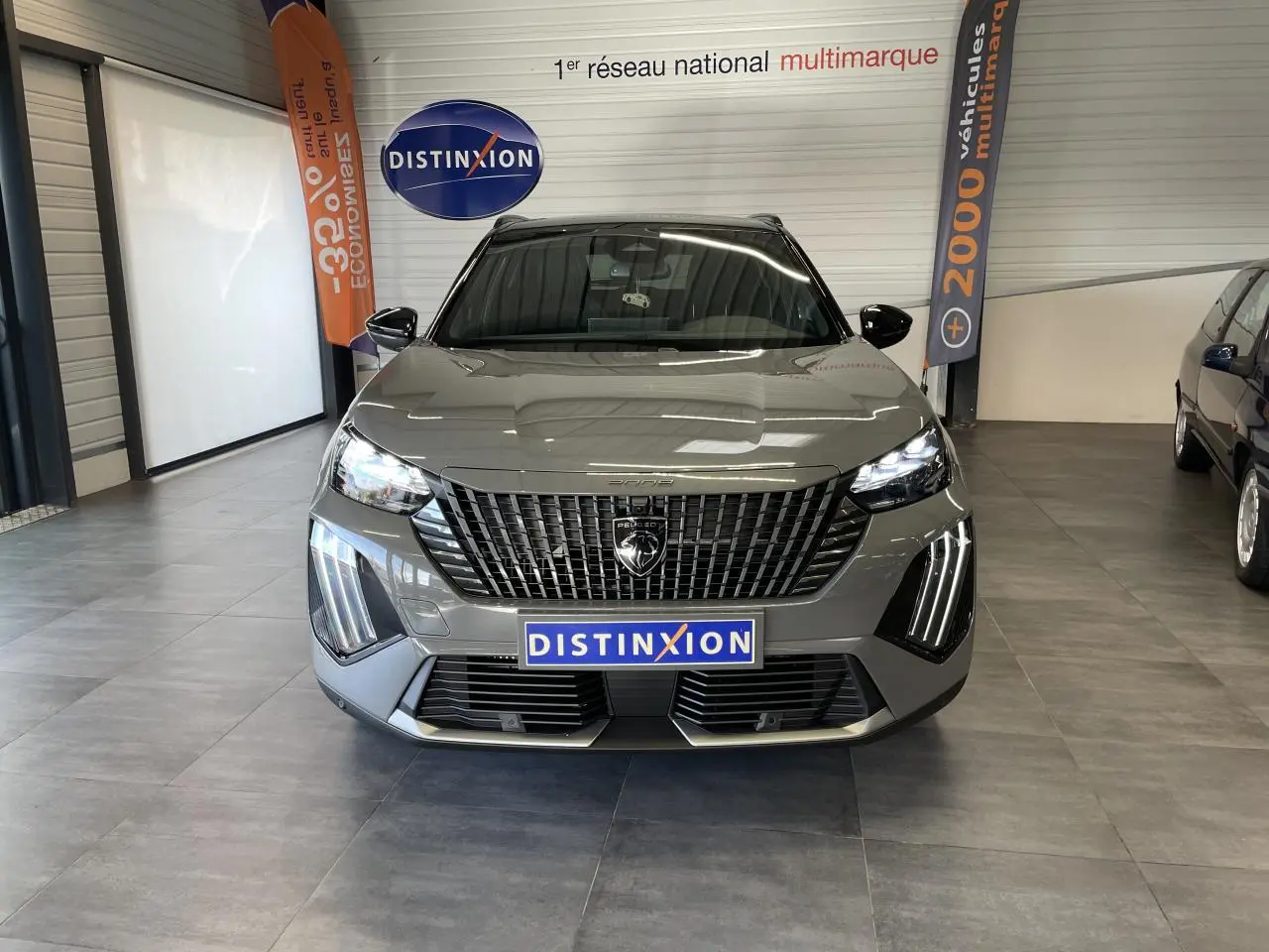 Peugeot 2008 gris en vue frontale, avec calandre noire distinctive et feux LED verticaux allumés en showroom.
