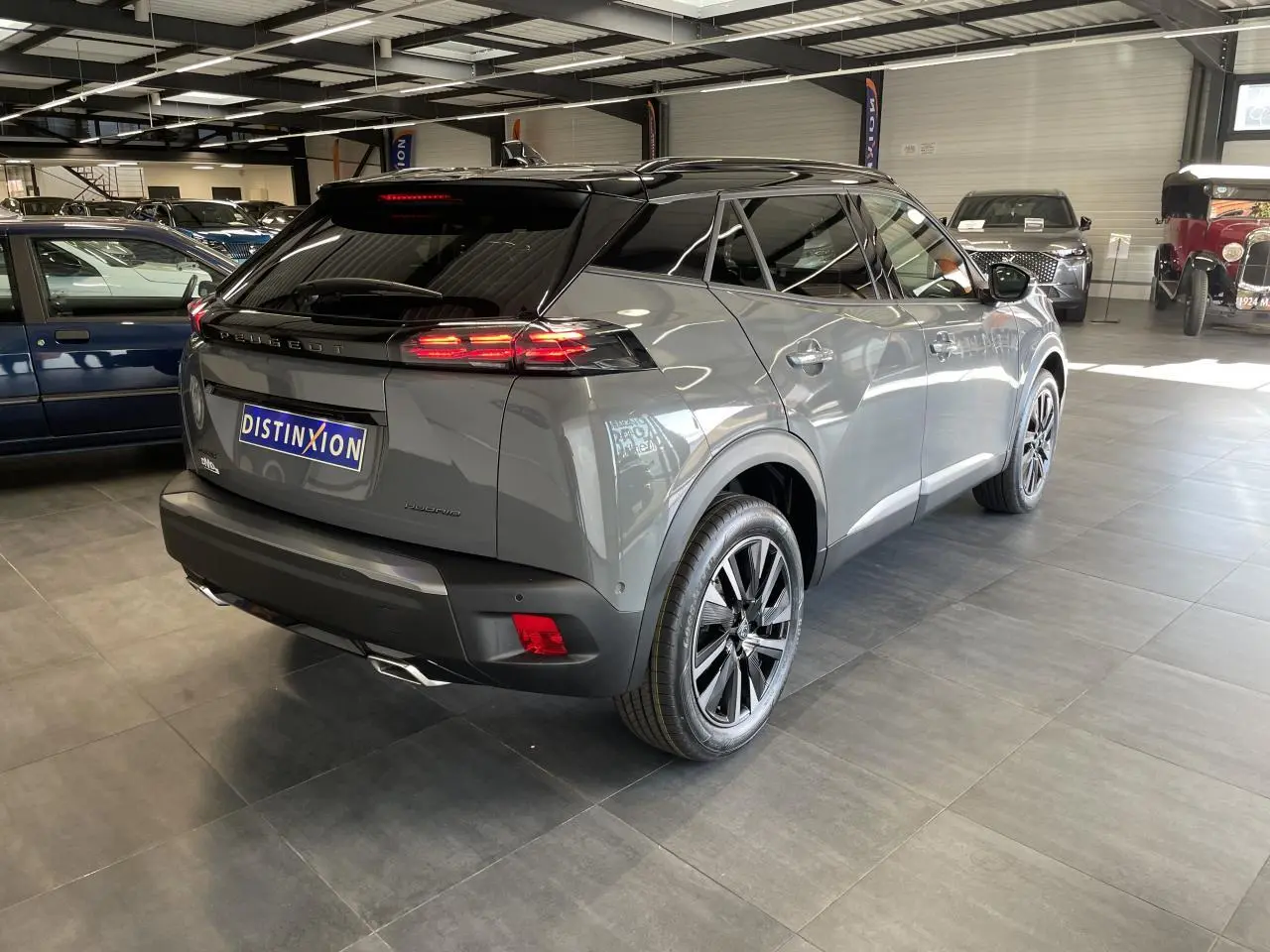 Peugeot 2008 gris en vue 3/4 arrière droit dans un showroom, avec toit noir et feux arrière allumés.
