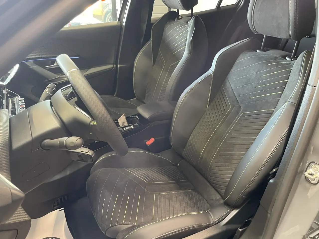 Vue intérieure côté conducteur du Peugeot 2008 gris 2026, sièges sport avec surpiqûres vertes et volant cuir.