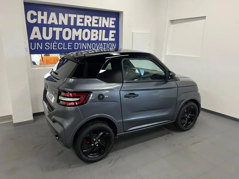 Vue 3/4 arrière droite d'une Ligier JS50 Sport Elite E5+ gris avec toit noir et jantes noires en intérieur showroom.