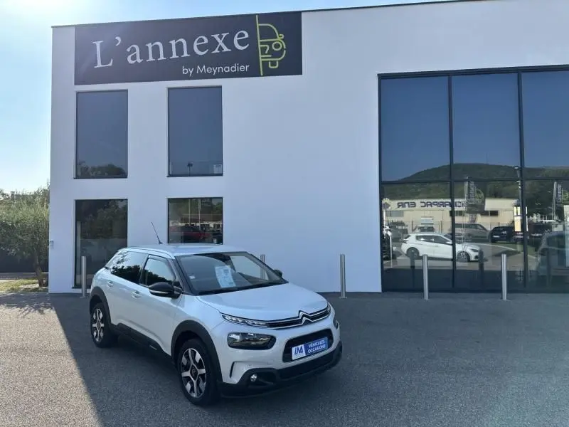 Citroën C4 Cactus blanc en 3/4 avant droit devant un bâtiment moderne avec grandes fenêtres réfléchissantes.