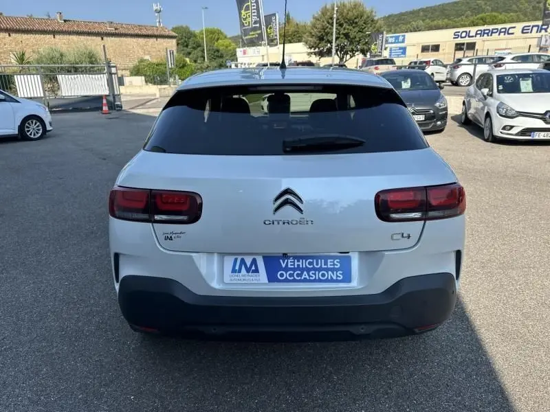 Vue arrière d'une Citroën C4 Cactus blanche de 2018 avec logo et feux rouges, stationnée en extérieur sur un parking.