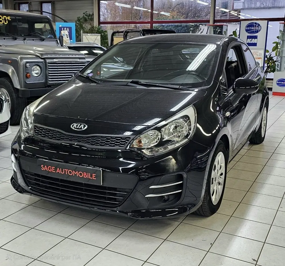 Vue 3/4 avant d'une KIA RIO III noire de 2015, compacte 3 portes avec phares larges et jantes blanches en showroom.