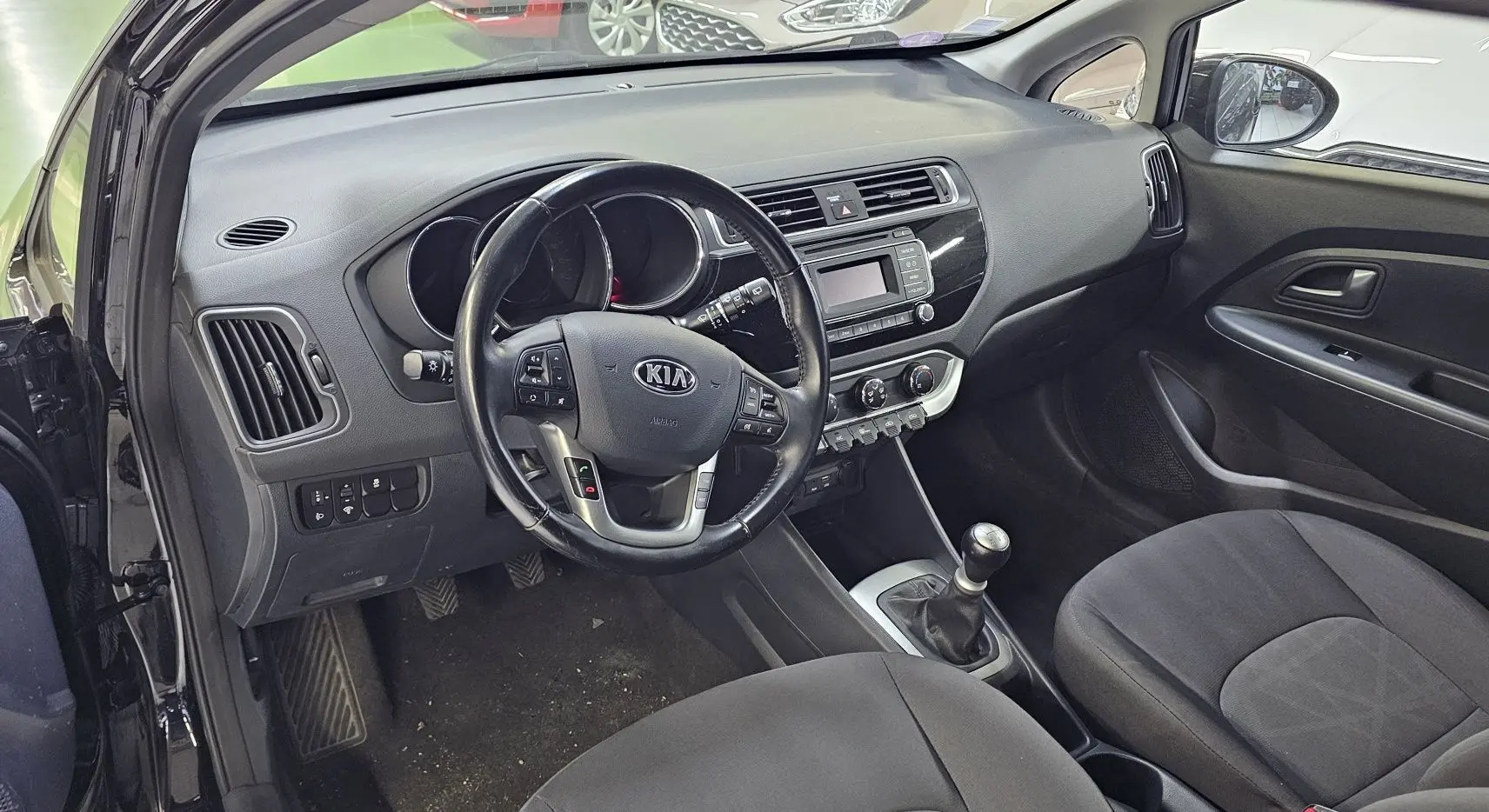 Intérieur de la KIA RIO III 2015 en noir, vue côté conducteur avec volant multifonction et boîte manuelle.