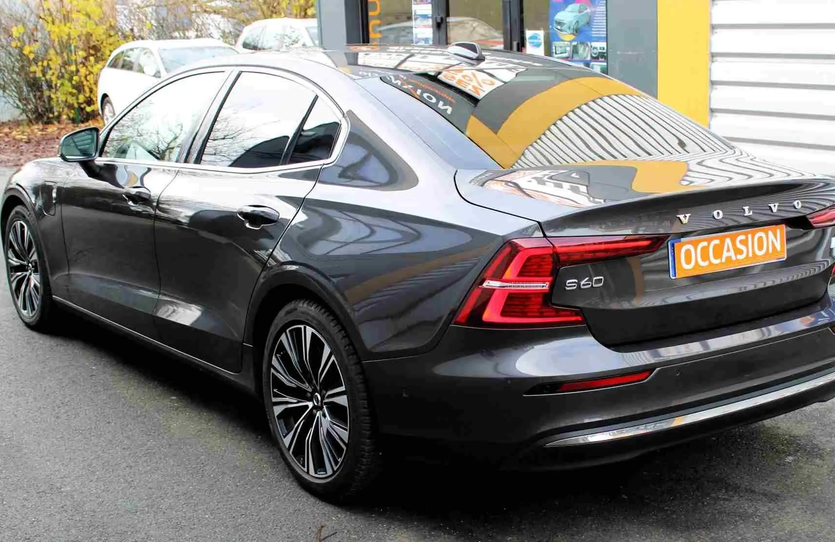 Vue 3/4 arrière droite d'une Volvo S60 gris métal 2024 avec jantes stylées et plaque "OCCASION" visible.