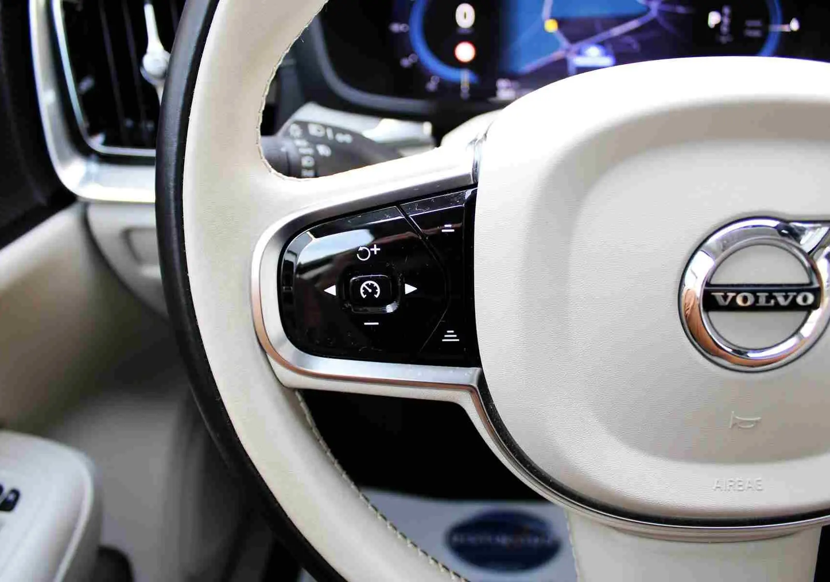 Gros plan sur le volant beige clair du Volvo S60 2024 avec commandes intégrées et logo chromé central.