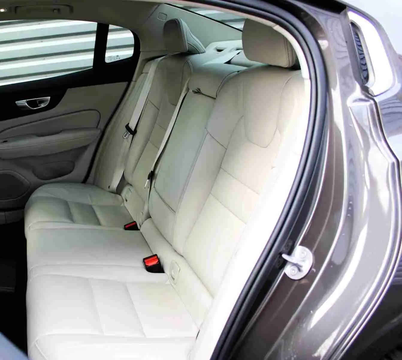 Vue côté droit sur l'intérieur arrière beige clair d'une Volvo S60 2024 gris métal avec sellerie cuir et ceintures visibles.