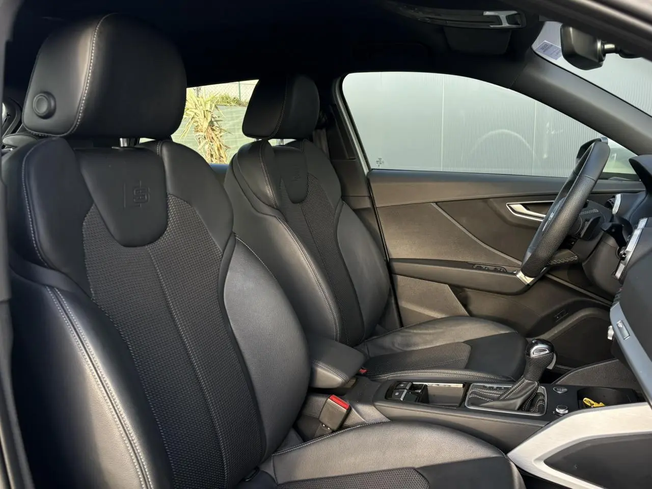 Vue intérieure côté conducteur de l'Audi Q2 35 TDI S-Line 2025 avec sièges sport cuir/tissu noirs et volant cuir.