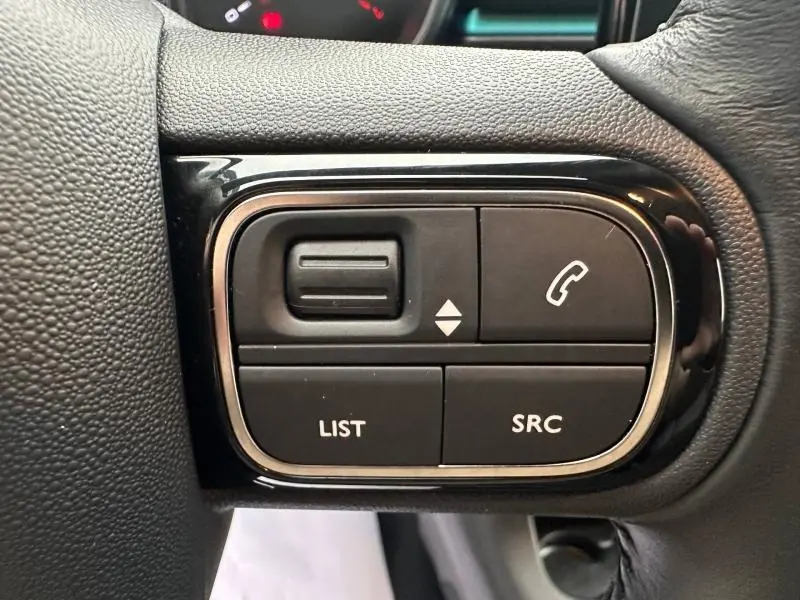 Gros plan sur les commandes multifonctions noires du volant de la Citroën C3 2023, finition Shine Spring Blue.