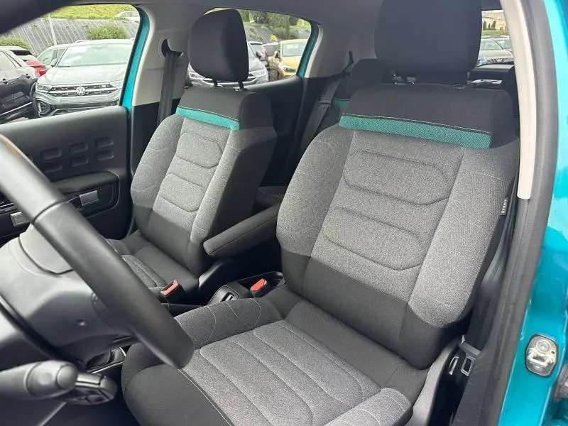 Vue intérieure de face des sièges avant gris avec bandeau bleu turquoise d'une Citroën C3 Spring Blue 2023, portière ouverte.