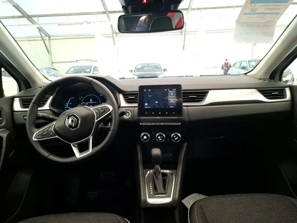 Vue intérieure frontale du tableau de bord du Renault Captur gris Highland 2023 avec écran tactile central et volant multifonction.