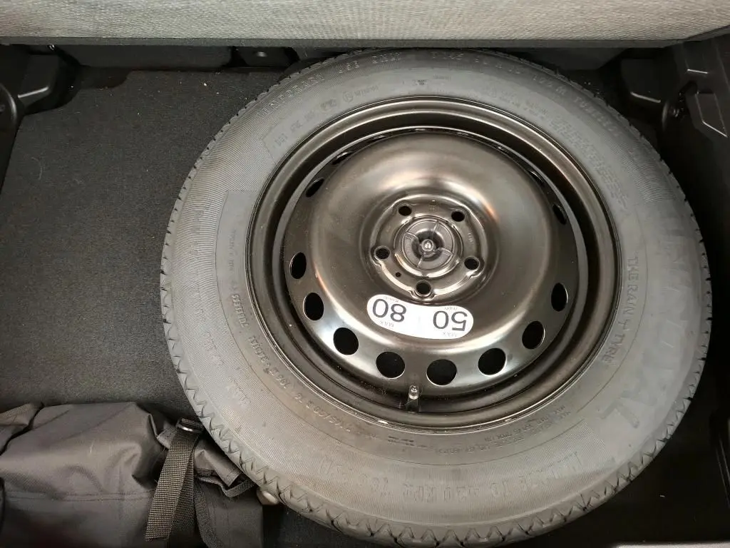 Vue plongeante sur la roue de secours noire en acier du coffre d'un Renault Captur gris Highland 2023.