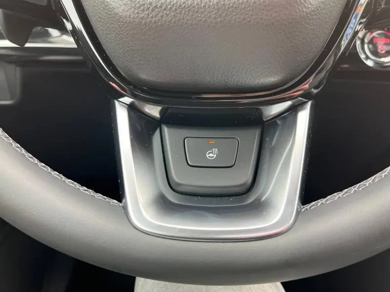 Gros plan sur le bouton de chauffage du volant noir et argent dans le Honda CR-V blanc platine nacrée 2024.