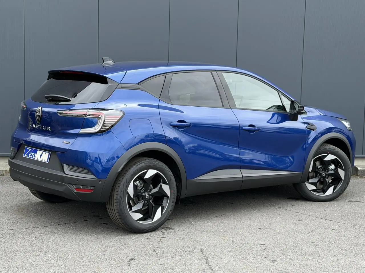 Renault Captur 2026 bleu Iron en vue 3/4 arrière droit, avec jantes aluminium noires et toit noir brillant.
