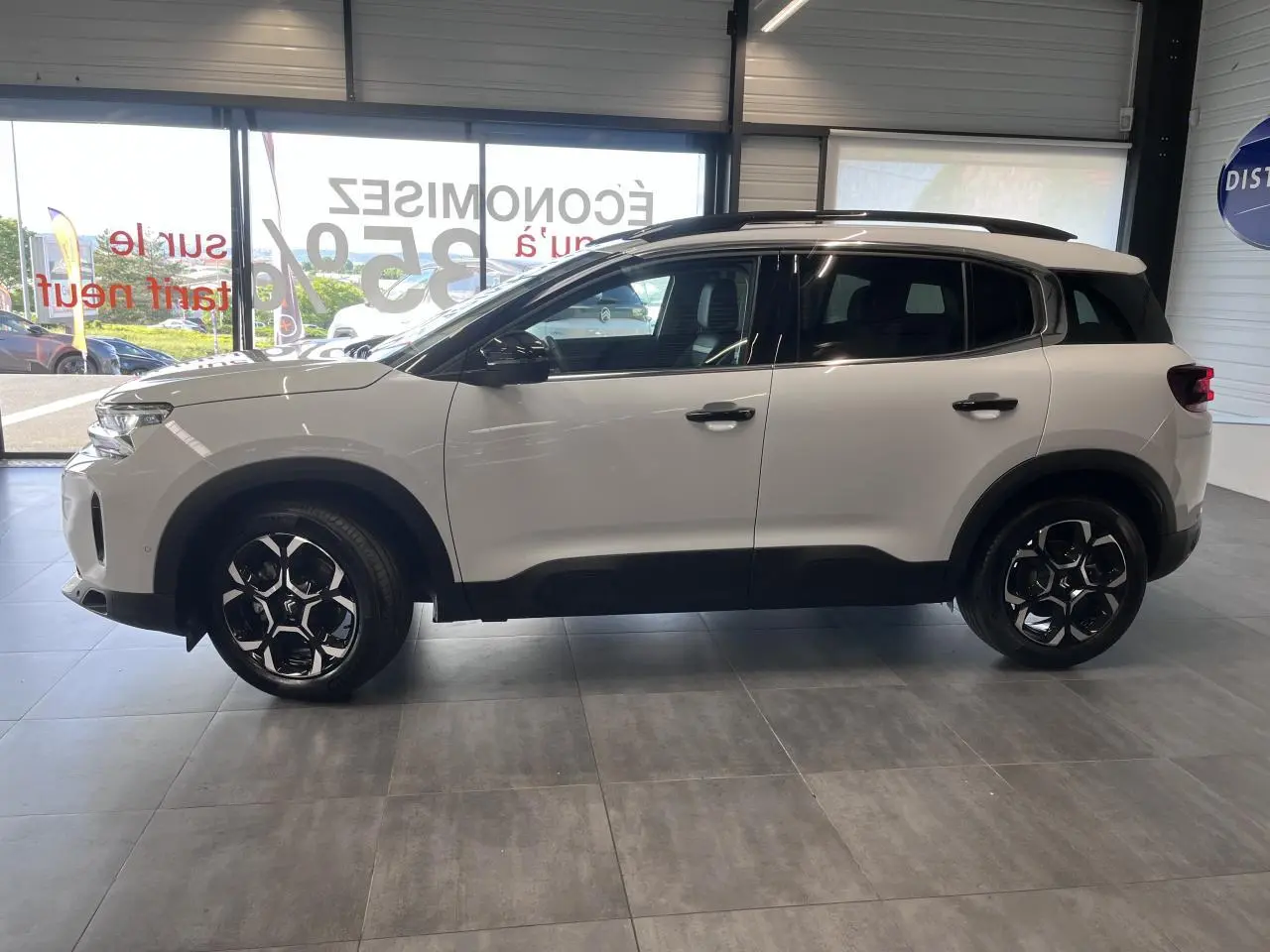 Vue latérale droite d'un Citroën C5 Aircross blanc nacré avec jantes alliage bi-ton et barres de toit noires.