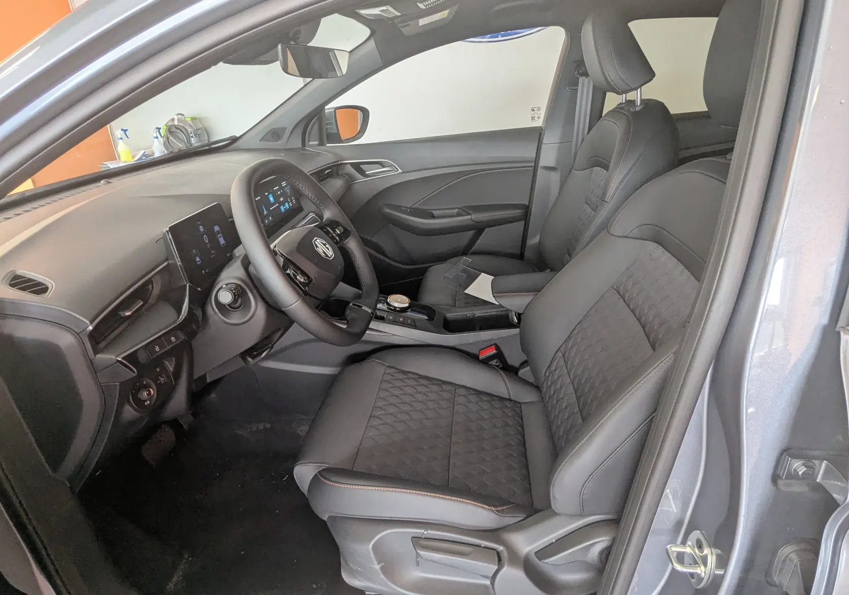 Vue intérieure côté conducteur de la MG3 1.5L Hybrid+ 2026 en gris Hampstead, sièges noirs avec surpiqûres orange et tableau de bord digital.
