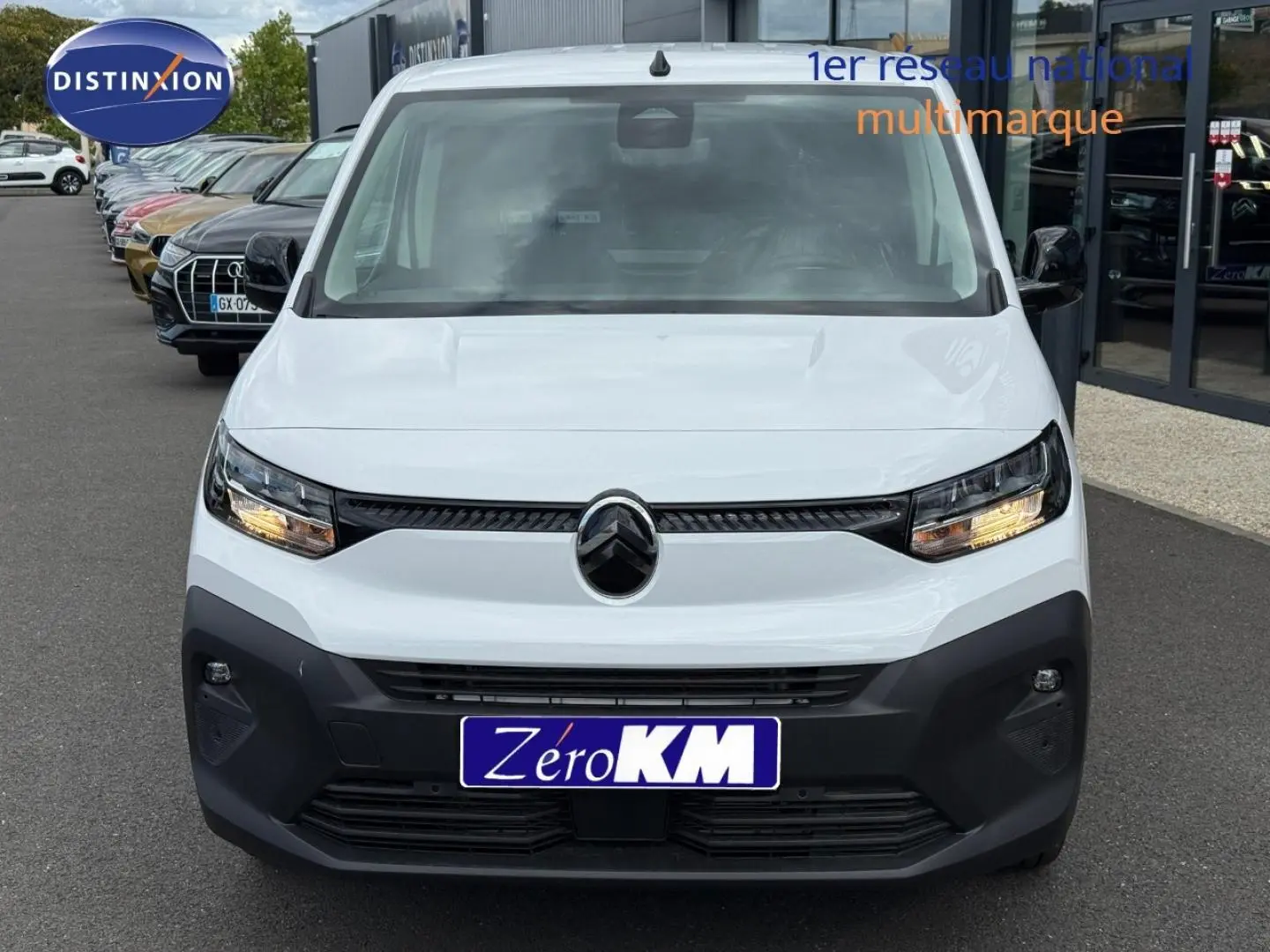 Vue frontale d'un Citroën Berlingo Fourgon XL Diesel 130ch blanc Icy avec phares allumés sur parking extérieur.