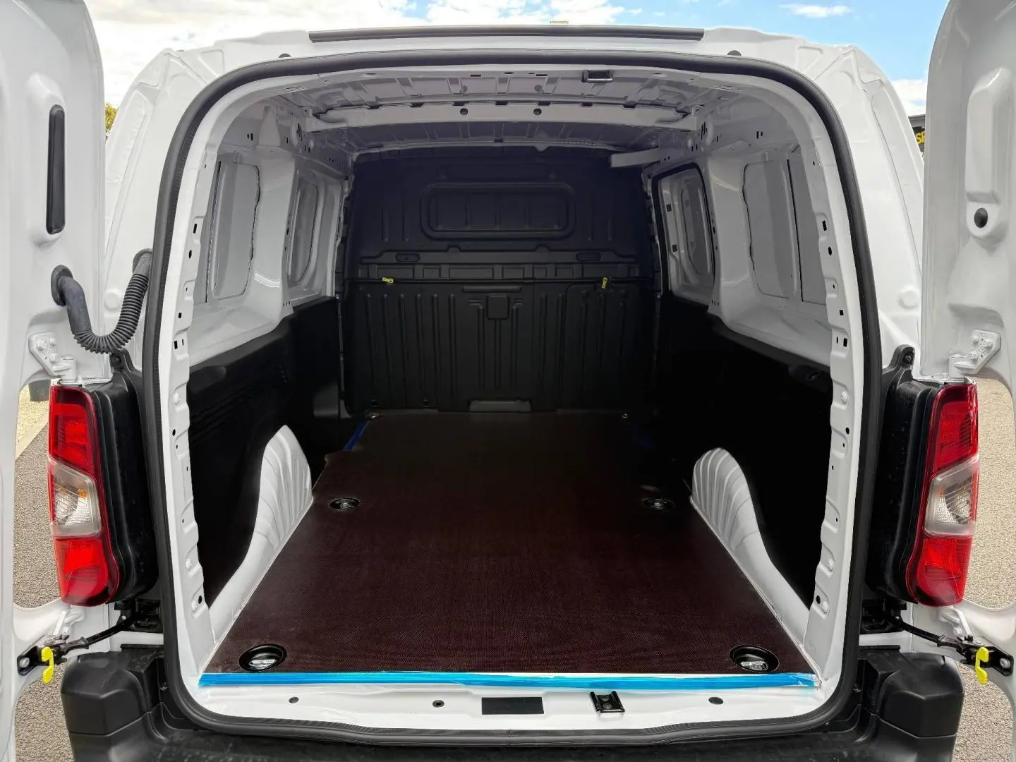Vue arrière ouverte du Citroën Berlingo Fourgon XL blanc Icy, montrant l’espace de chargement vide avec plancher en bois foncé.