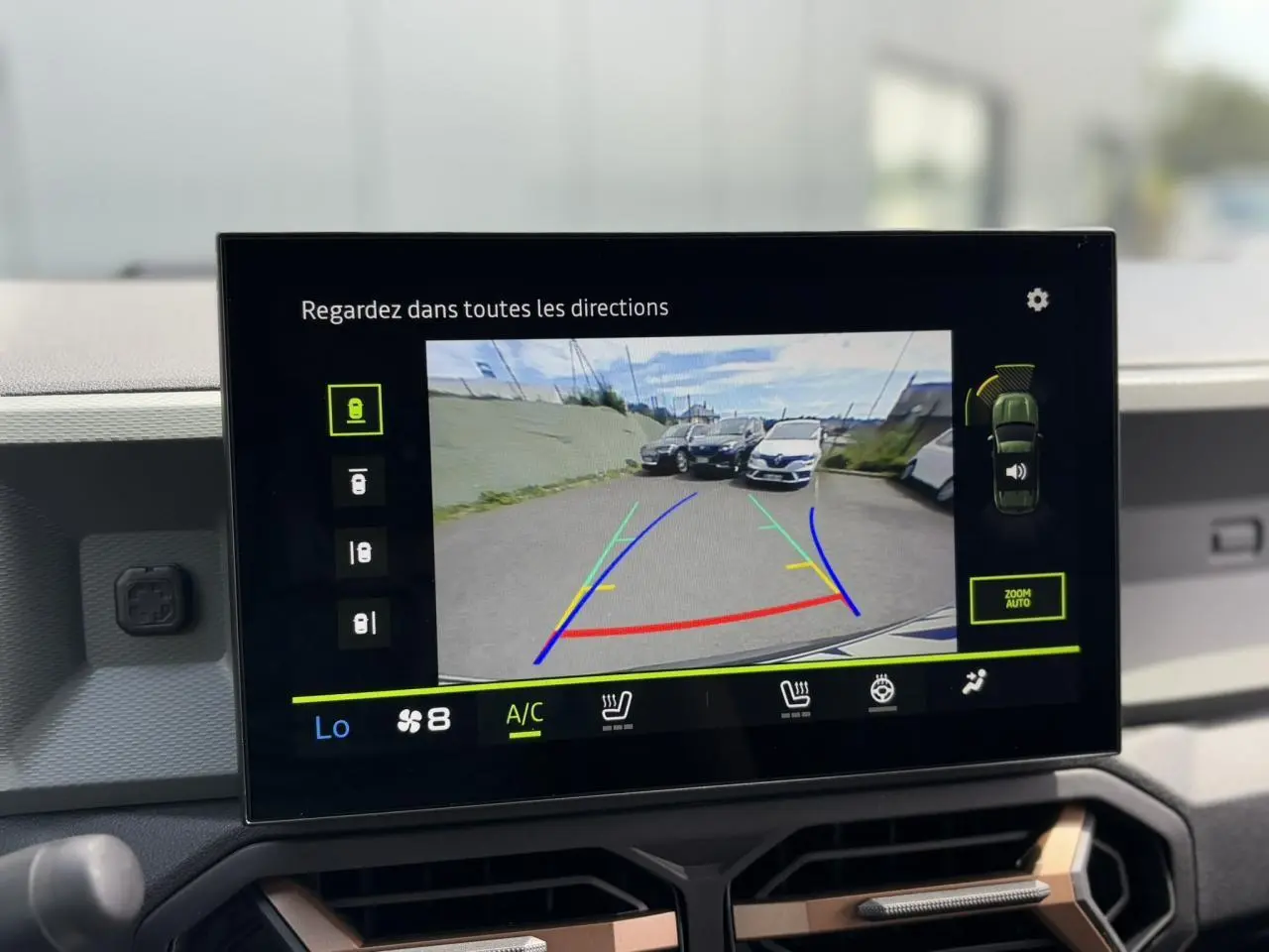 Écran tactile affichant la caméra de recul du Dacia Duster gris schiste avec lignes de guidage colorées.